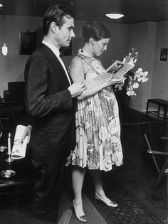 a man and woman standing next to each other in front of a table with flowers