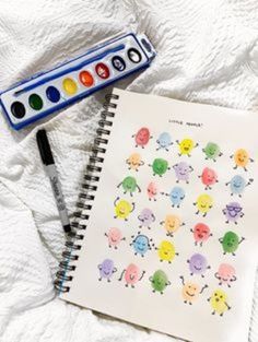 an open notebook with watercolors on it next to a paintbrush and marker