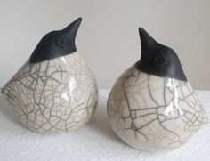 two ceramic birds sitting next to each other on a white tableclothed surface,