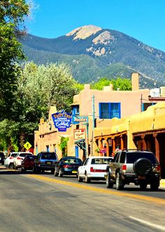 cars are parked on the side of the road in front of shops and buildings with mountains in the background