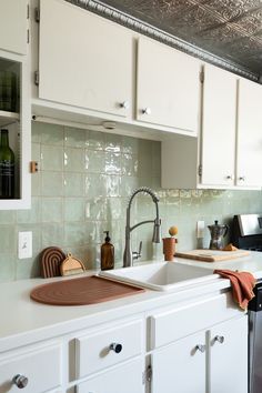 a kitchen with white cabinets and green tile backsplashing on the counter top