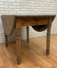 an old wooden table sitting on top of a hard wood floor next to a brick wall