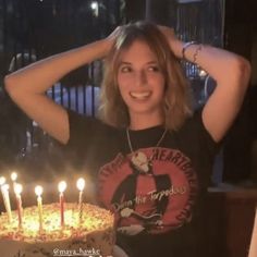 a woman standing in front of a birthday cake with lit candles on it and looking at the camera