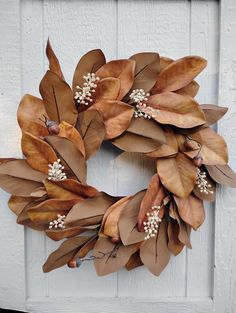 a wreath made out of leaves and flowers on a white wooden door with the words welcome