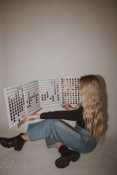 a woman is sitting on the floor with her legs crossed and looking at an array of earrings