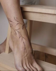 a woman's foot with a tattoo on the top of her left leg and leaves on it