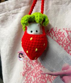 a small stuffed animal hanging from a red and green handle on a white tote bag