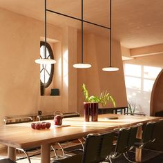 a dining room table with chairs and plants in vases on the table, along with hanging lights