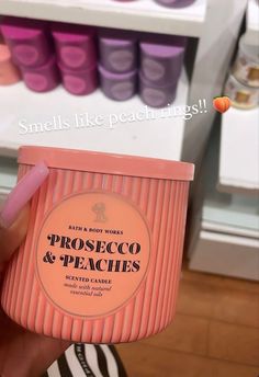 a person holding up a pink cup that says prosecco and peaches in front of shelves