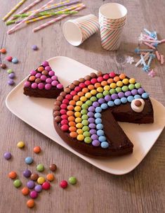 a chocolate cake decorated with rainbow candy and sprinkles on a white plate