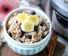 a bowl filled with oatmeal topped with bananas and raisins next to an instant rice cooker