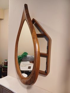 a wooden mirror hanging on the wall next to a shelf with shelves and drawers in it