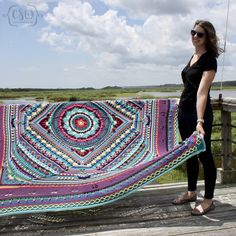 a woman standing on a deck holding up a colorful blanket that has been made into a quilt