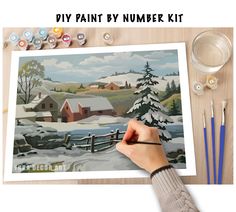 a person is painting a snowy scene with acrylic paint by number kit on a table