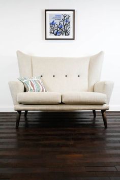 a white couch sitting on top of a hard wood floor next to a framed picture