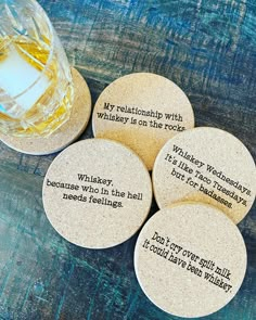 four cork coasters with quotes on them sitting next to a glass of whiskey and ice