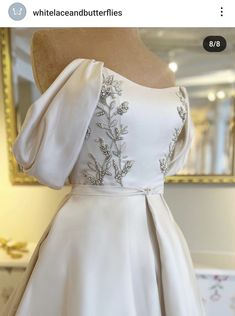 the back of a white dress on display in front of a gold framed mirror,