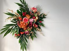 an arrangement of flowers and greenery is displayed on a white wall behind a vase