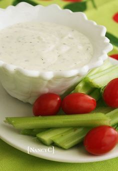 a white plate topped with celery and tomatoes next to a bowl of ranch dressing