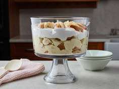 a dessert dish with bananas and whipped cream in it on a kitchen counter next to bowls