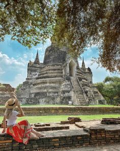 a woman sitting on top of a stone wall next to a large building with many spires