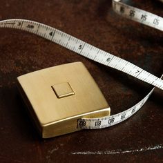 a gold square shaped object with a measuring tape around it's sides on a brown surface