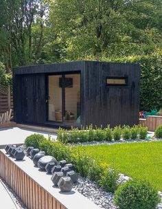 a small black building sitting in the middle of a yard next to a lush green field