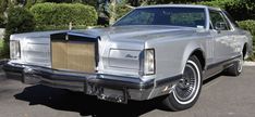 a silver car parked in a parking lot next to bushes and shrubbery on either side of the road