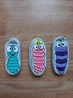 three painted rocks sitting on top of a wooden floor next to each other with cartoon characters