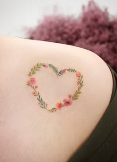 a heart shaped tattoo on the back of a woman's shoulder with pink flowers