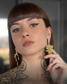 a woman with tattoos and piercings on her chest posing for the camera while wearing large gold earrings