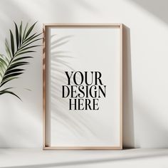 a white framed poster on a wall next to a potted palm plant with the words your design here