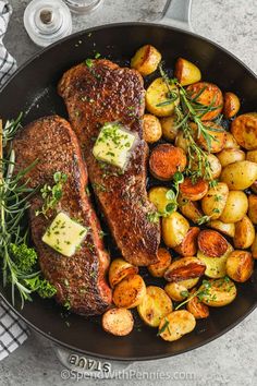 two steaks and potatoes in a skillet with herbs on the side for garnish