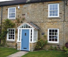 a blue door is in front of a stone building with white windows and green grass