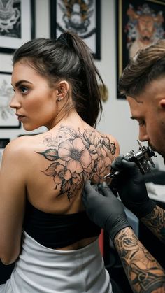 a woman getting a tattoo done by a man in a black and white dress with flowers on her back