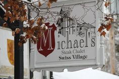 a white sign hanging from the side of a building next to a snow covered tree