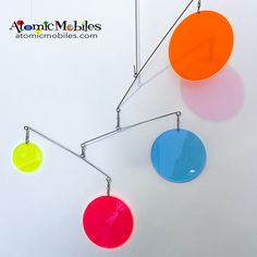 three colorful circles hanging from the ceiling in an art gallery with text overlay that reads, atomic mobiles