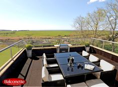 an outdoor dining table and chairs on a deck overlooking the green field in the distance