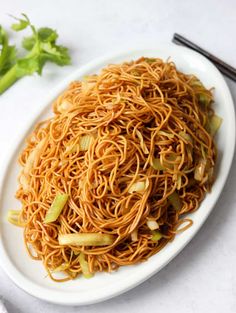 a white plate filled with noodles and vegetables next to chopsticks on a table