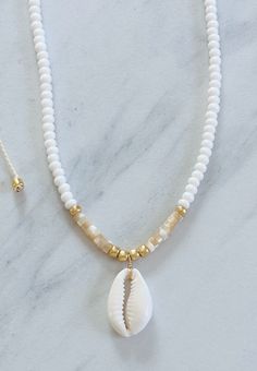 a white necklace with a shell on it and a gold beaded necklace hanging from the neck