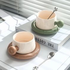 two coffee cups sitting on top of a table next to a book with spoons