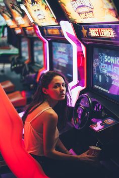 a woman sitting in front of a slot machine with neon lights on the sides and other machines behind her