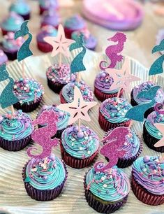 cupcakes decorated with pink and blue frosting are displayed on a plate in front of other cupcakes