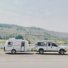 two white trucks parked next to each other on the side of a road near a body of water