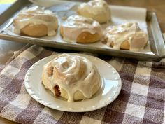 a white plate topped with cinnamon rolls on top of a checkered table cloth next to a tray