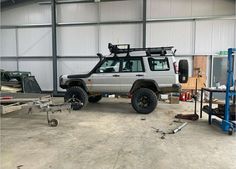 a jeep parked in front of a garage with tools on the ground and other vehicles