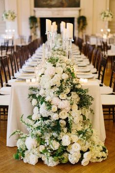 a long table with white flowers and candles on the top is set for a formal dinner