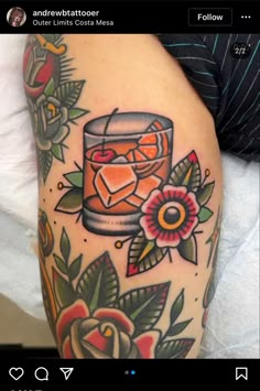 a woman's arm with an orange drink and flowers on it