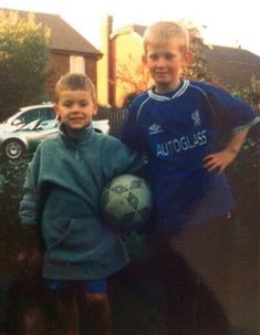 two young boys standing next to each other holding a soccer ball