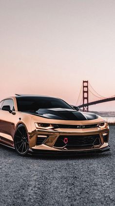 a gold chevrolet camaro is parked in front of the golden gate bridge at sunset